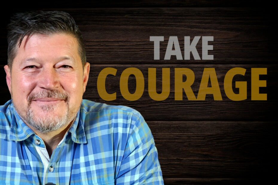 A Christian life coach smiling warmly in front of a rustic wooden background with the bold text "TAKE COURAGE," representing the power of Biblical Encouragement.